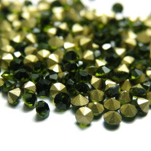 May include: A close-up of a pile of green and gold rhinestones. The rhinestones are small and have a faceted surface.