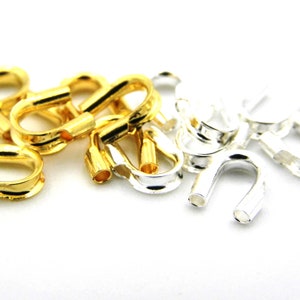 May include: A close-up of gold and silver metal jewellery findings. The findings are shaped like a U with a small loop at the top. They are used for making jewellery.