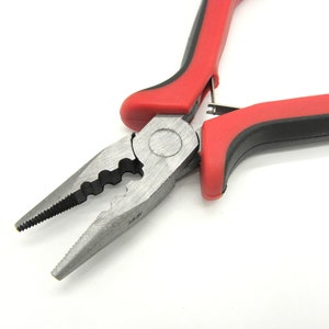 Op de afbeelding: Rode en zwarte tang met een zilveren metalen bek. De tang heeft een gekartelde rand en een veerbelaste handgreep.