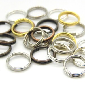 Op de afbeelding: Een verzameling split sleutelringen in diverse metallic afwerkingen, waaronder zilver, goud, brons en donker brons. De ringen zijn gerangschikt op een witte ondergrond, waarbij hun verschillende kleuren en texturen worden getoond. Ideaal voor knutselen en sieraden maken.