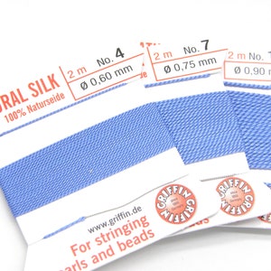 Könnte beinhalten: Drei Spulen mit blauem Naturseidenfaden zum Fädeln von Perlen und Perlen. Die Spulen sind mit der Fadenstärke in Millimetern beschriftet: 0,60 mm, 0,75 mm und 0,90 mm.