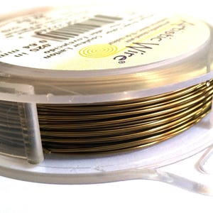 Peut inclure: Une bobine de fil de couleur or dans un récipient en plastique transparent. L'étiquette indique "Precious Wire" et indique la taille du fil comme étant de 26 AWG, 0,4 mm.