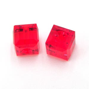May include: Two faceted, bright red, square-shaped objects. The objects are transparent and appear to be made of a crystal-like material. They are set against a white background. The objects have a geometric design.
