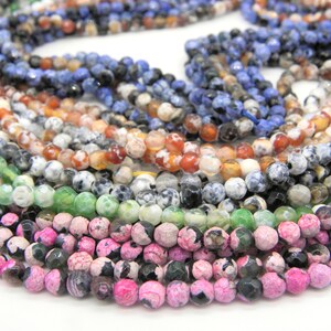 May include: A collection of gemstone beads in various colors, including pink, green, blue, orange, and black. The beads are round and faceted, strung together to form necklaces or strands. The image showcases a variety of natural stone beads.