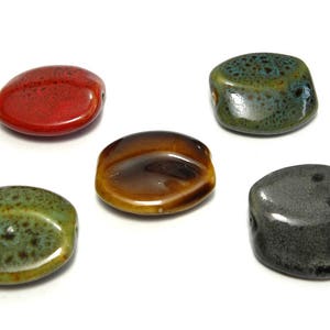 Può includere: Cinque perline ovali in ceramica di diversi colori e motivi. Le perline sono rosse, marroni, verdi, grigie e blu.