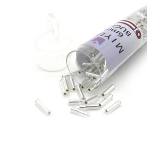 Könnte beinhalten: Ein durchsichtiges Plastikröhrchen gefüllt mit silberfarbenen Metallperlen. Das Röhrchen ist mit "MIYU 6mm Buckles" beschriftet.