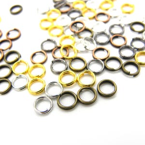 Peut inclure: Un assortiment de petits anneaux ouverts de différentes finitions métalliques, dont l'or, l'argent, le bronze et le canon de fusil. Ces composants de fabrication de bijoux sont dispersés sur un fond blanc, mettant en valeur leurs couleurs et textures.