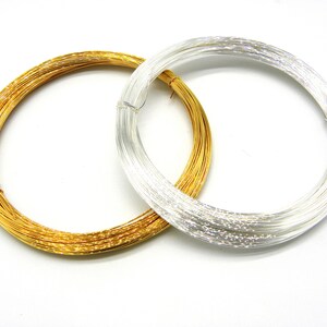 May include: Two spools of wire, one gold and one silver, are coiled in a circle. The spools are on a white background.