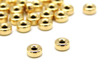 Könnte beinhalten: Ein Haufen goldfarbener Metallperlen mit runder Form und einem Loch in der Mitte. Die Perlen sind in einem zufälligen Muster angeordnet.