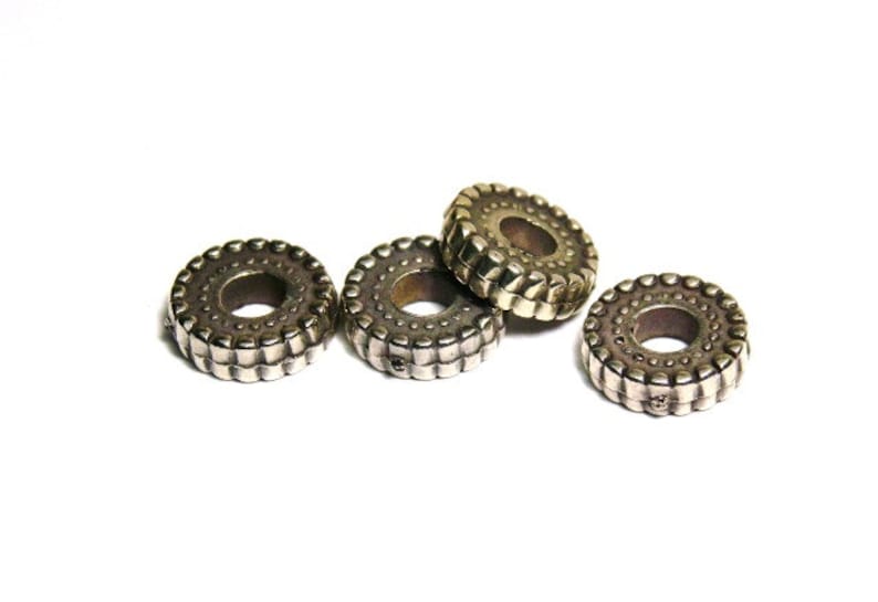 May include: Four silver-toned metal rings with a textured design. The rings are circular in shape with a hole in the centre.