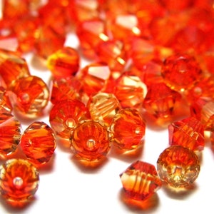 May include: A collection of faceted orange beads with a glossy, transparent appearance. The beads are scattered, showcasing their various shapes and sizes, reflecting light and creating a vibrant display. Ideal for jewelry making or craft projects.