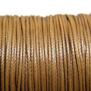 Op de afbeelding: Close-up van een spoel bruin gewaxt koord. Het koord is strak opgerold en vertoont een getextureerd oppervlak. De kleur is een warm, aards bruin, geschikt voor diverse knutselprojecten.