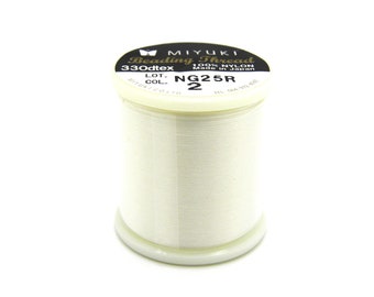 Può includere: Una bobina di filo per perline Miyuki bianco sporco. L'etichetta recita "Beading Thread" e "100% Nylon Made in Japan". La bobina è cilindrica con una base e un coperchio in plastica bianca. Il filo è ben avvolto e sembra liscio.