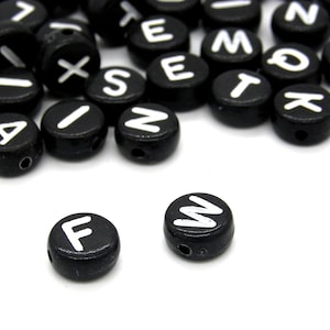 May include: Black wooden letter beads with white letters. The letters are F, W, A, I, X, S, T, N, M, O, K, E, and more.