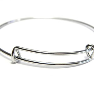 Op de afbeelding: Een zilveren, verstelbare armband met een eenvoudig, open ontwerp. De armband is gemaakt van metaal en heeft een gladde afwerking.