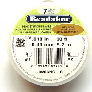 Op de afbeelding: Een spoel Beadalon kralenrijgdraad. Het etiket geeft een diameter van 0,46 mm en een lengte van 9,2 m aan. De draad is satijn goudkleurig en is bedoeld voor volwassenen.