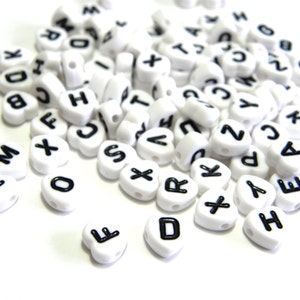May include: White heart-shaped beads with black letters of the alphabet. The beads are scattered on a white surface.