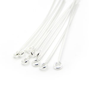 May include: A close-up of a bundle of silver-toned head pins with a loop at one end. The pins are arranged in a fan shape.