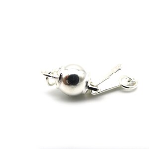 Może przedstawiać: Srebrne zapięcie do biżuterii, prawdopodobnie do naszyjnika lub bransoletki, na białym tle. Zapięcie posiada okrągły, kulisty element i zawiasowe zamknięcie dźwigniowe. Metal ma jasne, odblaskowe wykończenie.