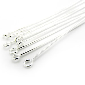 May include: A close-up of a group of silver head pins with eye loops. The pins are arranged in a fan shape, with the eye loops facing the viewer.