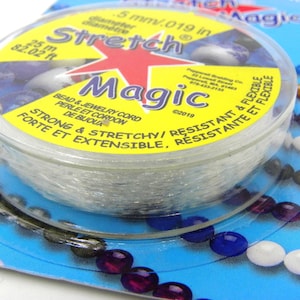 Könnte beinhalten: Eine transparente, aufgerollte Stretchschnur für die Schmuckherstellung, mit der Aufschrift "Magic". Die Verpackung ist gelb und blau, mit Text, der darauf hinweist, dass die Schnur 0,5 mm Durchmesser, 25 m lang, stark und dehnbar ist.