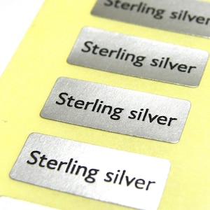 Puede incluir: Cuatro etiquetas rectangulares plateadas con el texto "Sterling silver" impreso en negro.