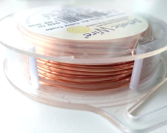 Może przedstawiać: Widoczna jest szpula drutu Artistic Wire w kolorze miedzianym, 1 oz, 1,02 mm średnicy. Drut jest ciasno nawinięty na przezroczystą plastikową szpulę. Etykieta zawiera logo Artistic Wire i napis "Artistic Wire".
