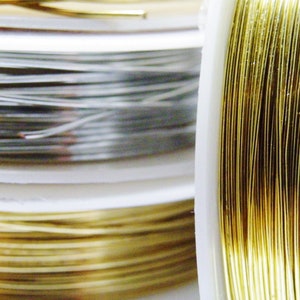 Könnte beinhalten: Zwei Spulen mit Draht, eine silberne und eine goldene, sind fest um weiße Kunststoffspulen gewickelt.
