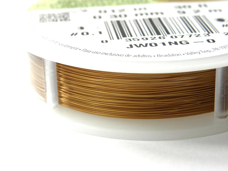 Op de afbeelding: Een spoel goudkleurig draad voor het maken van sieraden. De spoel is gelabeld "JW01NG-0" en heeft een barcode.