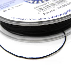 Può includere: Una bobina di filo nero per perline, con un diametro di 0,3 mm, è visibile su sfondo bianco. La bobina di plastica trasparente ha testo stampato in bianco e blu. Il filo è etichettato come "no stretch Xtra strong".