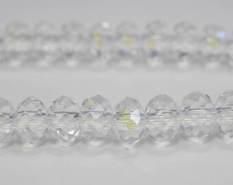 Könnte beinhalten: Zwei Stränge aus klaren, facettierten Kristallperlen. Die oval geformten Perlen sind aufgereiht und reflektieren das Licht. Der Hintergrund ist eine schlichte, weiße Oberfläche. Ideal für die Schmuckherstellung.