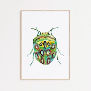Op de afbeelding: Een aquarel schilderij van een groene, gele en rode kever met zwarte stippen. De kever is realistisch afgebeeld en is ingelijst in een eenvoudige houten lijst.