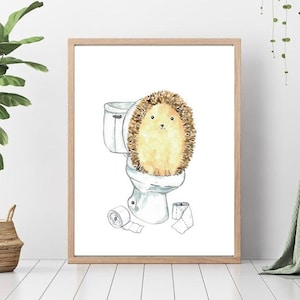 Puede incluir: Una ilustración de acuarela de un erizo sentado en un inodoro con rollos de papel higiénico en el suelo. El erizo es marrón y tiene la barriga blanca. El inodoro es blanco y tiene un asiento azul.