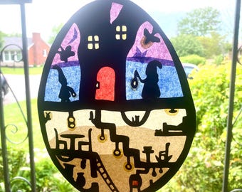 May include: A black paper cutout of a house with a red door and windows, surrounded by a colorful background of blue, purple, and pink. The house is set against a backdrop of a brown, winding path with yellow lights.