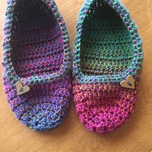 May include: A pair of crocheted slippers with a gradient of pink, purple, blue, and green. Each slipper has a wooden heart button.