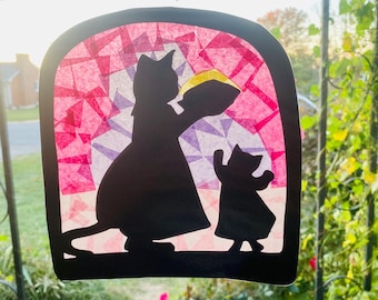 May include: A black silhouette of a cat holding a yellow object, with a smaller cat reaching up, set against a stained-glass style background of pink and purple geometric shapes. The artwork is framed by a black border, creating a charming, whimsical scene.