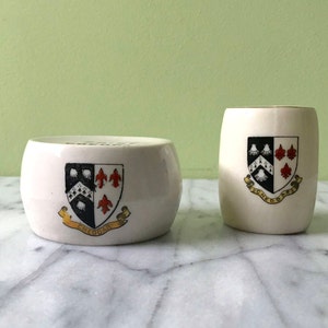 May include: Two white ceramic containers with a gold trim. Both containers feature a black and white crest with red accents. The crest on the larger container says "Cheddar".