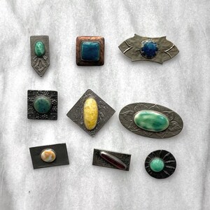 May include: Assortment of ten vintage enamel and metal brooches with various colors and designs. The brooches feature a variety of shapes, including squares, ovals, and diamonds.