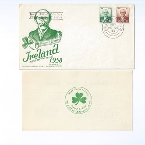 May include: A 1958 Irish first day cover envelope featuring a green illustration of Thomas J. Clarke, a shamrock, and the text Ireland First Day of Issue 1958. Two postage stamps are affixed with a circular postmark. The back shows a green shamrock seal.