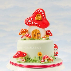 Op de afbeelding: Een groene en witte taart versierd met rode en witte paddenstoelkoekjes en een rood en wit paddenstoelhuiskoekje. Een klein dwergfiguurtje staat op de taart.