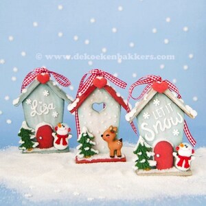 May include: Three white wooden houses with red roofs and red hearts on the front. The houses are decorated with white snowflakes and have a red door. The houses are sitting on a white snowy surface. The houses are decorated with the words "Lisa", "Let It Snow", and a reindeer.