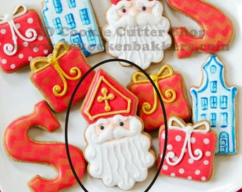 Könnte beinhalten: Ein Set aus neun Lebkuchen, die mit Zuckerguss verziert sind. Die Kekse sind in Form von Häusern, Geschenken und einer Sinterklaas-Figur. Die Kekse liegen auf einem weißen Teller.
