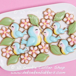 May include: A plate of decorated sugar cookies featuring blue birds, green leaves, and pink flowers. The cookies are decorated with royal icing and are arranged in a pleasing pattern.  &copy; 3D Cookie Cutter Shop www.dekoekenbakkers.com