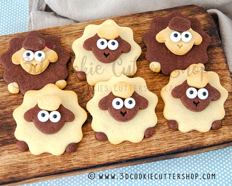 May include: Six brown and white sugar cookies shaped like sheep with black eyes and white icing. The cookies are arranged on a wooden chopping board.