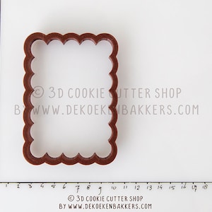 May include: Brown plastic cookie cutter shaped like a square with a scalloped edge. The cutter is approximately 7.5 cm wide and 7.5 cm tall.