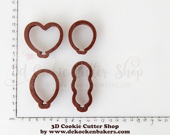 May include: Four brown plastic cookie cutters in the shape of a heart, two balloons, and a wavy line. The cutters are on a white surface with a ruler marked in centimeters.