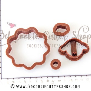 May include: A set of four brown plastic cookie cutters. The cutters are shaped like a flower, a sheep, and two circles. The cutters are on a white surface with a ruler in the background.