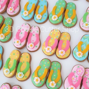 Op de afbeelding: Assortiment van kleurrijke flip-flop-vormige suikerkoekjes, versierd met verschillende patronen en bloemen. 3D Cookie Cutter Shop.