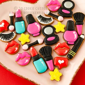 Op de afbeelding: Een verzameling koekjes in de vorm van make-up items, waaronder lippenstift, nagellak en oogschaduw, gerangschikt op een hartvormige schaal. De koekjes zijn versierd met roze, zwarte, witte en turquoise glazuur.