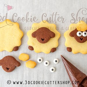 May include: Three decorated sugar cookies shaped like sheep. The cookies are decorated with brown and yellow icing and white candy eyes. The cookies are on a white surface. The image also shows a piping bag with brown icing and additional cookie pieces.